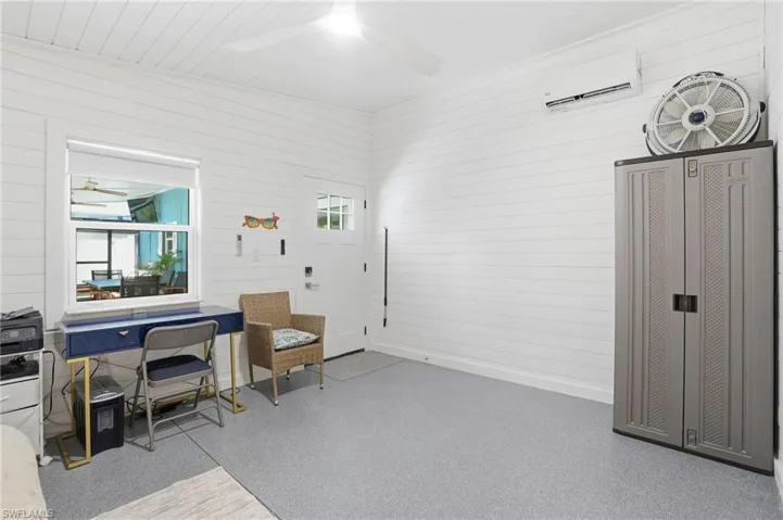 Office area featuring wooden walls, ceiling fan, and a wall mounted air conditioner - Virtually Edited Image