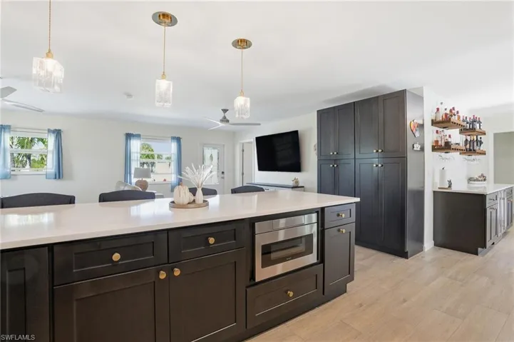Kitchen with decorative light fixtures, light wood tile flooring, stainless steel microwave, and light stone counters - Virtually Edited Image