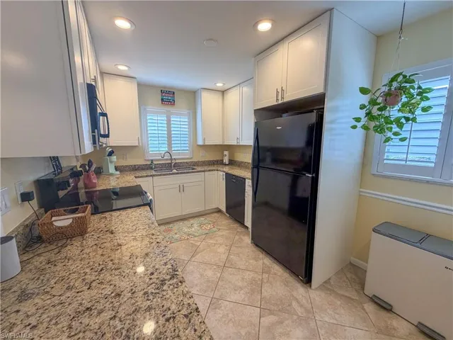 Kitchen featuring white cabinets, light stone counters, black appliances, recessed lighting, and light tile patterned floors