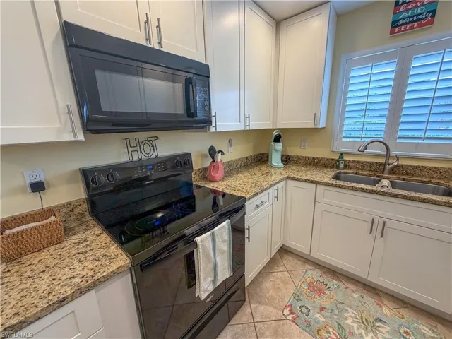 Kitchen with black appliances, white cabinets, light stone counters, and light tile patterned floors