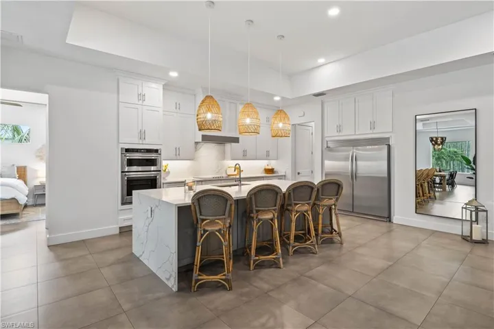 Kitchen featuring stainless steel appliances, a center island with sink,breakfast bar, tile flooring, and decorative light fixtures