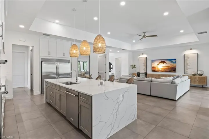 Kitchen featuring a center island with sink, a raised ceiling, hanging light fixtures, center island sink and custom white cabinetry with Quartz waterfall center island feature.