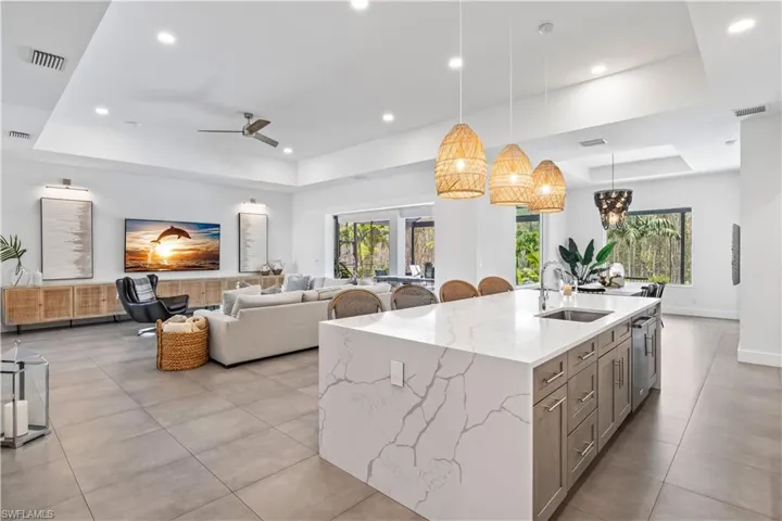 Kitchen with a tray ceiling, light Quartz  counters, hanging light fixtures and a kitchen island with sink