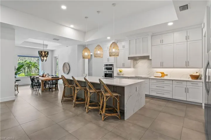 Kitchen with a tray ceiling, tasteful backsplash, an island with sink, decorative light fixtures, and white cabinets