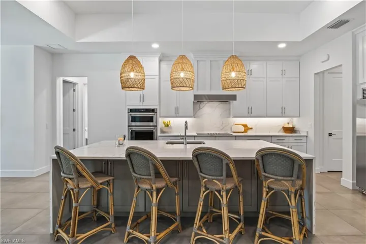 Kitchen featuring hanging light fixtures, an island with sink, double oven, sink, and light tile floors