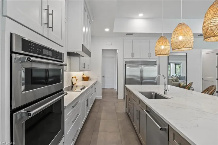 Kitchen with dark tile floors, stainless steel appliances, pendant lighting, sink, and white cabinetry