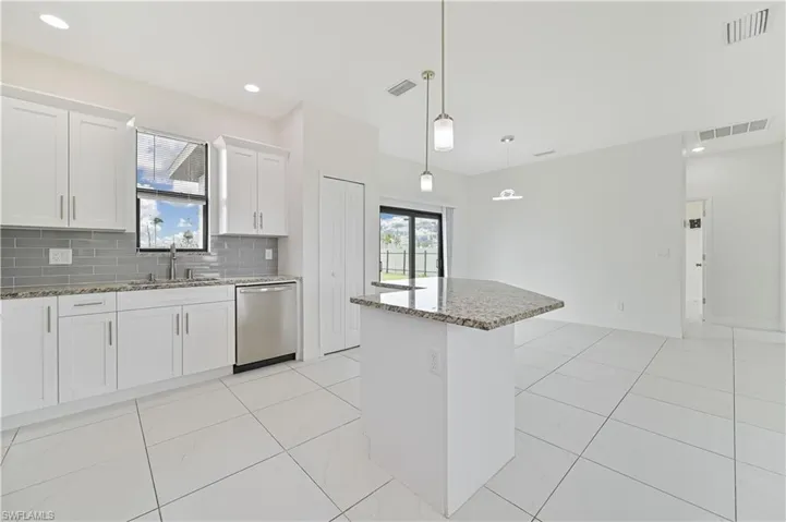 Kitchen featuring light stone countertops, white cabinetry, stainless steel dishwasher, backsplash, and pendant lighting
