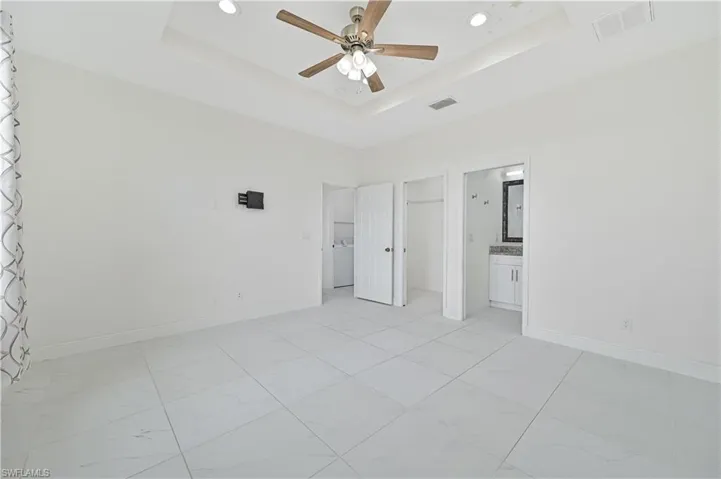 Primary bedroom with a spacious walk in closet, a ceiling fan, a raised ceiling, and connected primary bathroom