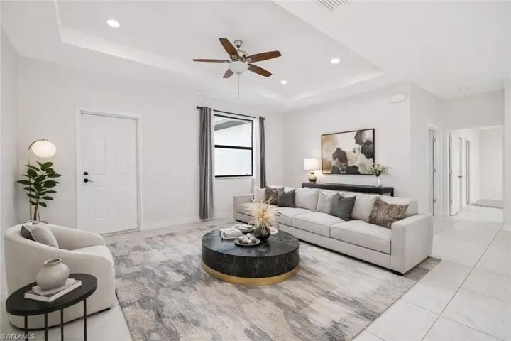 Virtually staged living room with a ceiling fan, a raised ceiling, recessed lighting, and light tile patterned floors.  Light, bright open concept