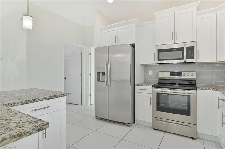 Kitchen with stainless steel appliances, light stone countertops, white cabinetry, tasteful backsplash, and pendant lighting
