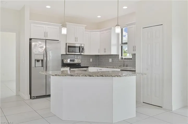 Kitchen with stainless steel appliances, white cabinetry, a center island, light stone countertops, and decorative backsplash