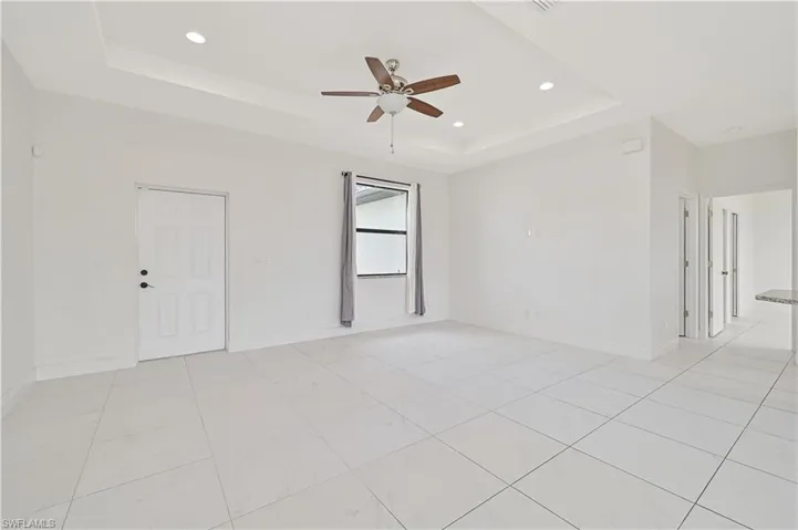 Ceiling fan, a raised ceiling, light tile patterned floors, and recessed lighting