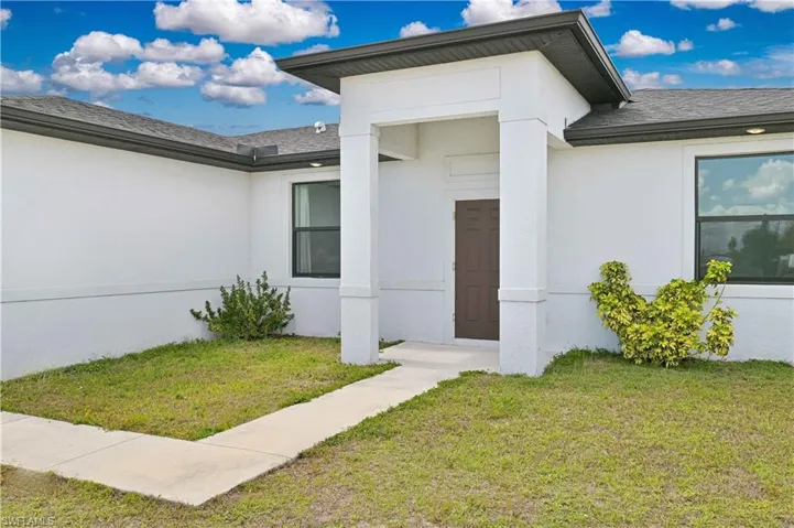 Entrance to property featuring a yard, stucco siding, and roof with shingles