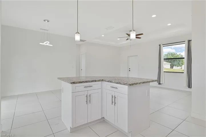 Kitchen with white cabinets, decorative light fixtures, light stone counters, a raised ceiling, and a kitchen island