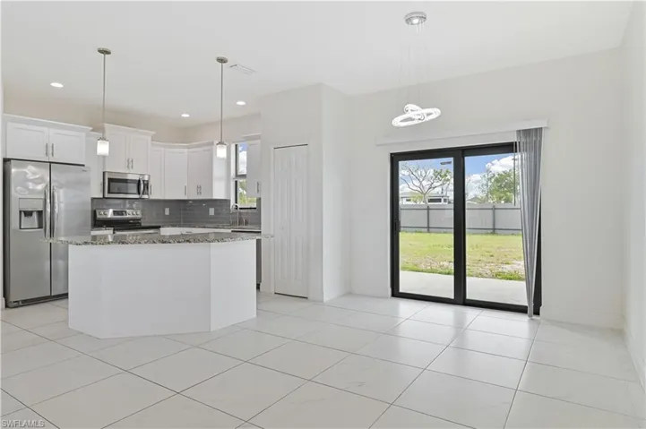 Kitchen with stainless steel appliances, light stone counters, white cabinets, backsplash, and a kitchen island