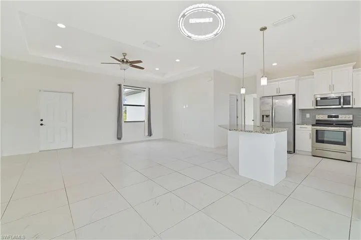 Kitchen featuring stainless steel appliances, a kitchen island, white cabinets, tasteful backsplash, and light stone counters