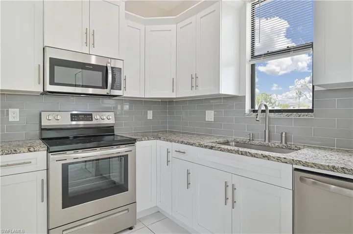 Kitchen featuring stainless steel appliances, white cabinets, light stone counters, backsplash, and light tile patterned flooring