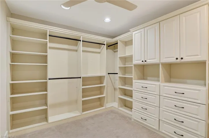 Walk in closet with a ceiling fan and light colored carpet
