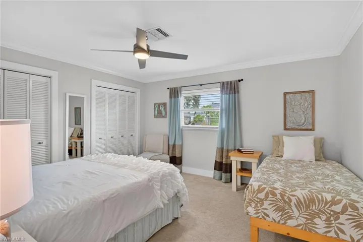 Bedroom with two closets, light carpet, crown molding, and a ceiling fan
