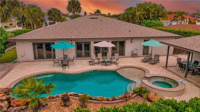 Pool at dusk with french doors, outdoor dining area, a patio area, and a pool with connected hot tub