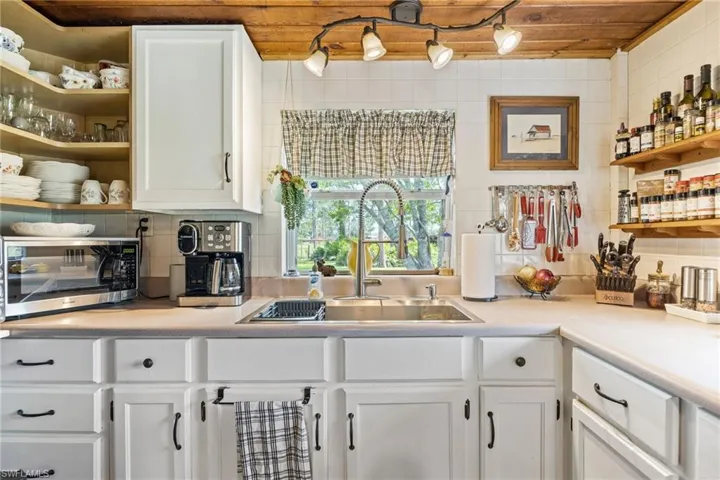 Kitchen featuring stainless steel microwave, open shelves, white cabinets, tasteful backsplash, and light countertops