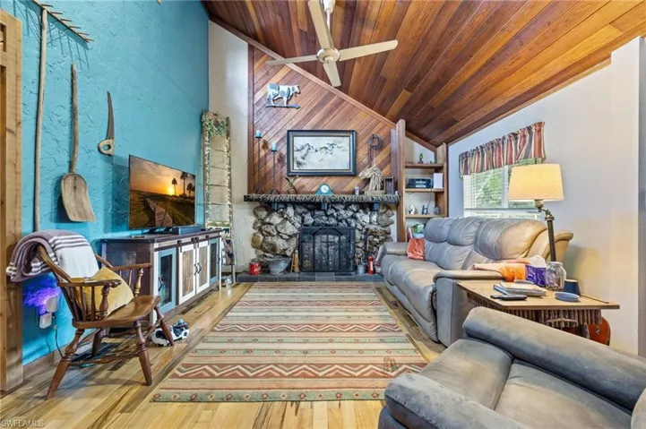 Living room with wooden ceiling, lofted ceiling, wood finished floors, ceiling fan, and a fireplace