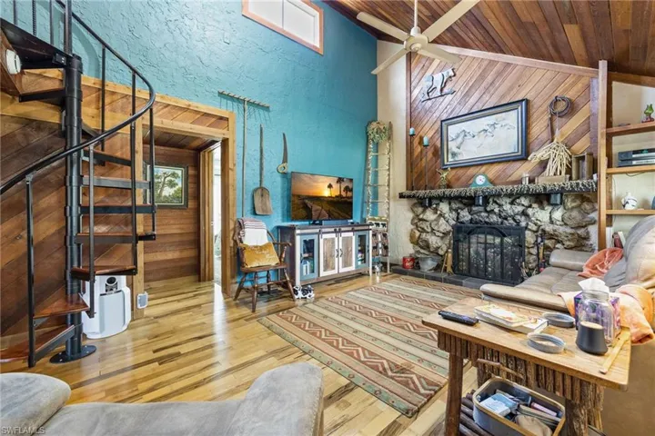 Living room with wood ceiling, wood-type flooring, wood walls, a stone fireplace, and ceiling fan