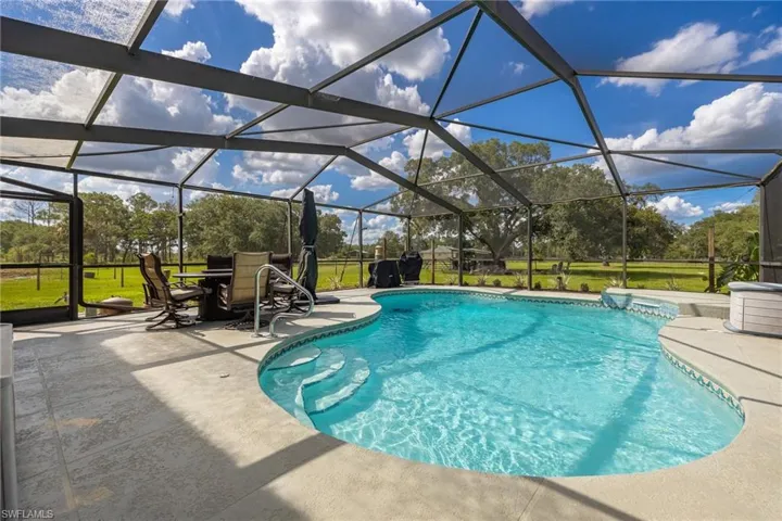 Swimming pool with a patio area, view of scattered trees, a lanai, and a lawn
