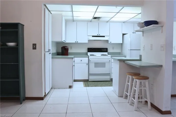 Kitchen with white appliances, under cabinet range hood, white cabinets, a breakfast bar area, and a peninsula