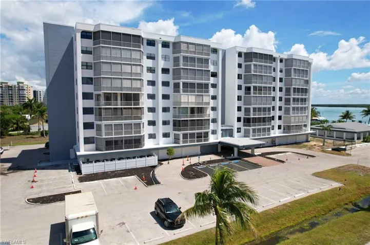 Multi-story residential building featuring a covered entrance portico, exterior balconies with screen enclosures, and an asphalt parking lot