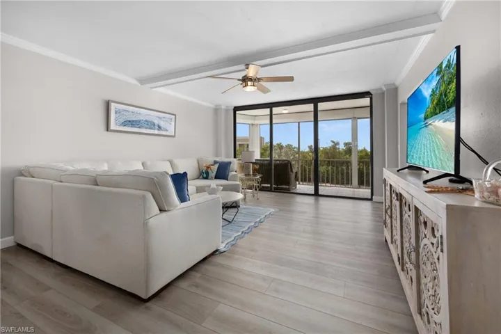 Living area featuring wood-finish flooring, a ceiling fan with integrated lighting, crown molding, and floor-to-ceiling sliding glass doors opening to a screened balcony