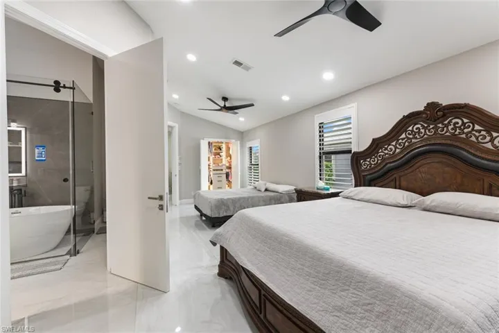 Bedroom featuring ensuite bathroom, lofted ceiling, a ceiling fan, recessed lighting, and light marble finish floors
