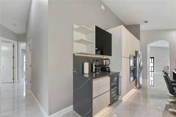 Kitchen featuring open shelves, arched walkways, light wood finish cabinets, modern cabinets, and wine cooler