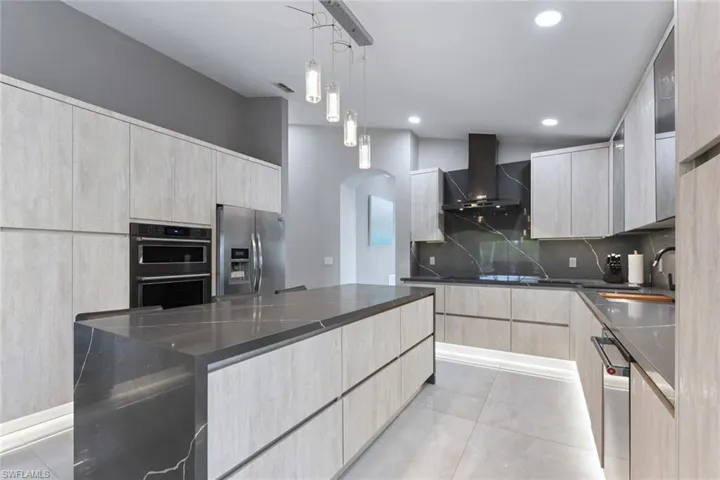 Kitchen featuring light wood finish cabinets, stainless steel appliances, dark stone counters, and decorative light fixtures