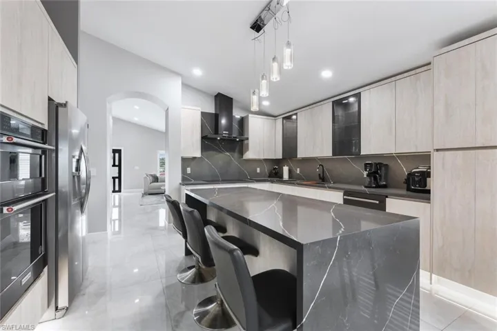 Kitchen featuring a breakfast bar area, modern cabinets, dark stone counters, decorative light fixtures, and black appliances