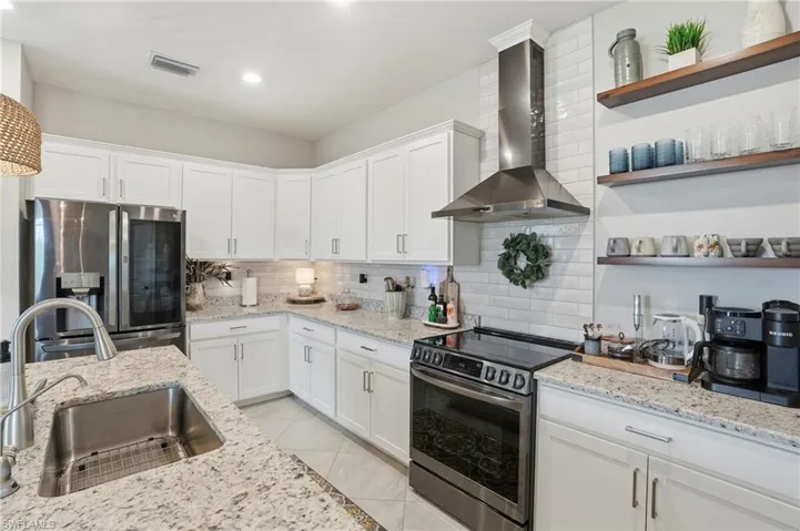 Kitchen with stainless steel appliances, exhaust hood, white cabinets, and recessed lighting