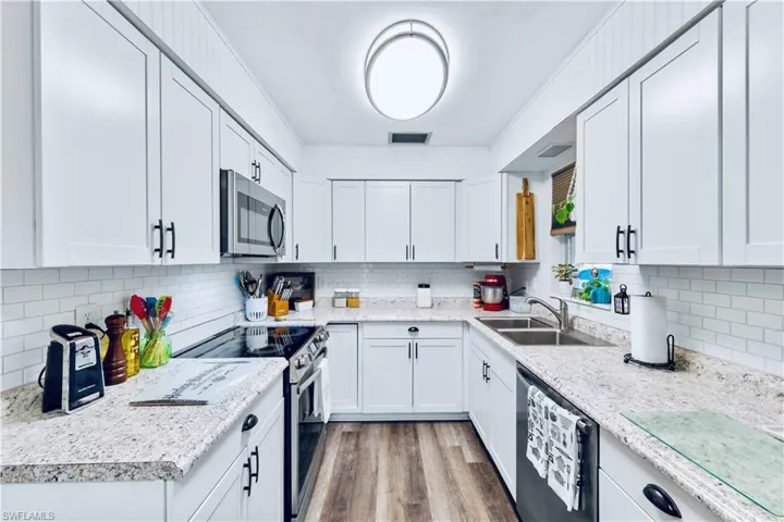 Kitchen featuring white cabinetry, sink, stainless steel appliances, backsplash, and light wood-type flooring