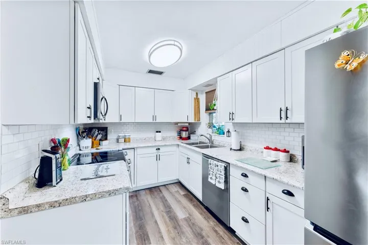 Kitchen with white cabinets, decorative backsplash, stainless steel appliances, and light hardwood / wood-style flooring