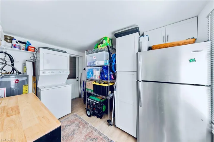 Kitchen with white cabinetry, stainless steel refrigerator, stacked washer / dryer, and light hardwood / wood-style flooring