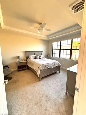 Carpeted bedroom with a tray ceiling, ceiling fan, and ornamental molding