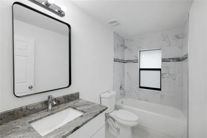 2nd full bath featuring granite vanity, shower / bath combination, and marble look tiles