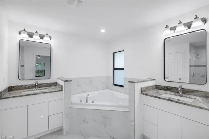 Primary bathroom featuring a garden tub, two granite vanities, a shower stall, light marble finish floors, and recessed lighting