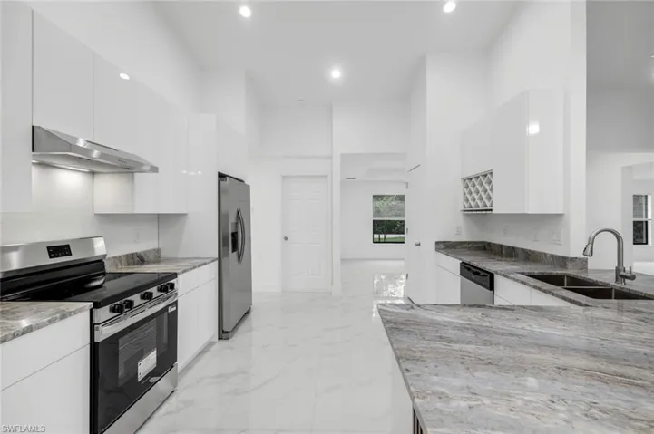 Large kitchen featuring stainless steel appliances, granite countertops, modern cabinets, white cabinetry, and recessed lighting