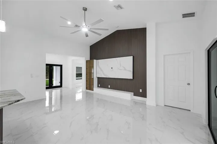 Great room with an accent wall, high vaulted ceiling, light marble finish floors, and ceiling fan view towards front door