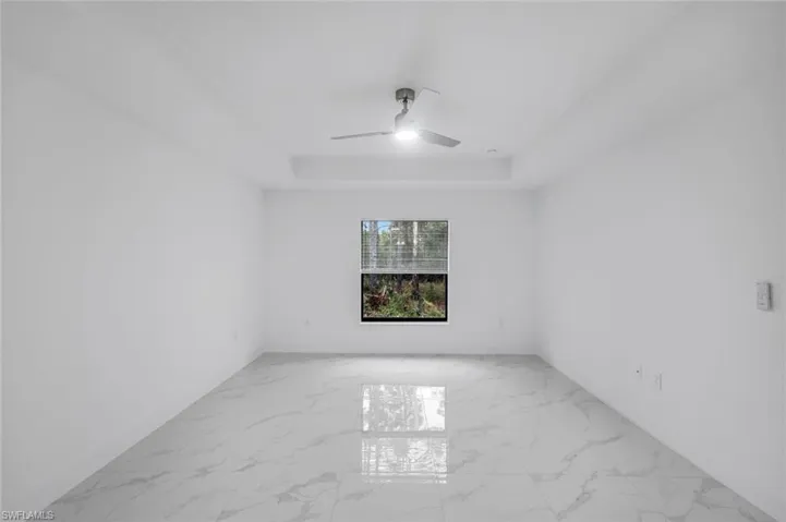 Bedroom 2 with light marble finish floors, a tray ceiling, and a ceiling fan