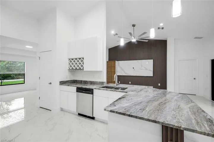 Kitchen featuring light marble finish floors, granite counters, high vaulted ceiling, door to the pantry