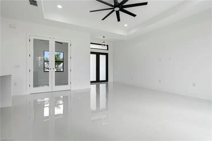 Tiled empty room featuring french doors, a tray ceiling, and ceiling fan