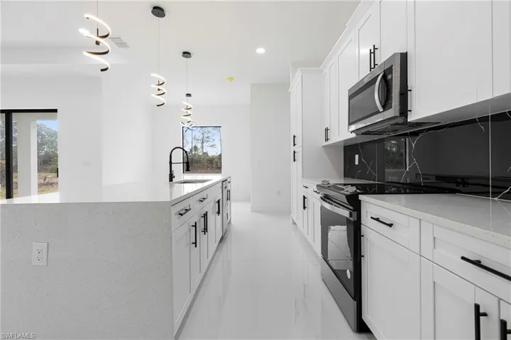 Kitchen with decorative backsplash, appliances with stainless steel finishes, sink, decorative light fixtures, and white cabinetry