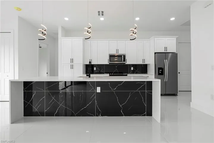 Kitchen with pendant lighting, white cabinets, sink, decorative backsplash, and stainless steel appliances
