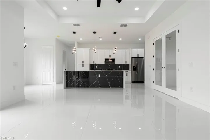 Kitchen featuring white cabinets, light tile patterned floors, appliances with stainless steel finishes, tasteful backsplash, and decorative light fixtures